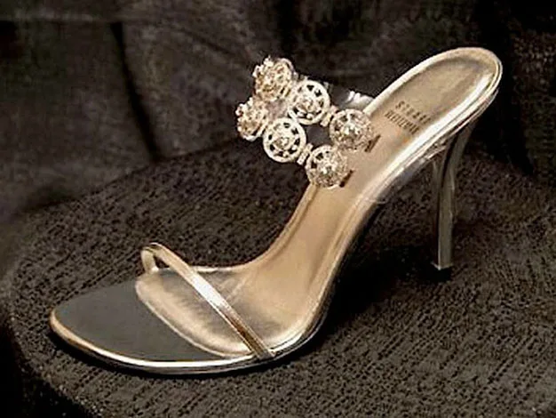 Silver high-heeled sandal with intricate crystal decoration on a dark textured background.