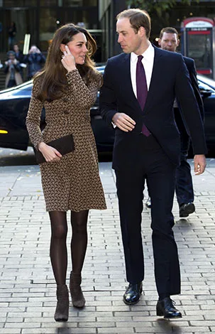 A man and woman walking together, with the woman in a patterned dress and the man in a dark suit and purple tie.
