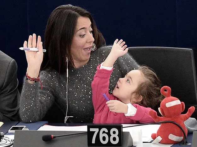 Woman and child share a playful moment, raising hands, seated at desk with number 768; red toy sits nearby.