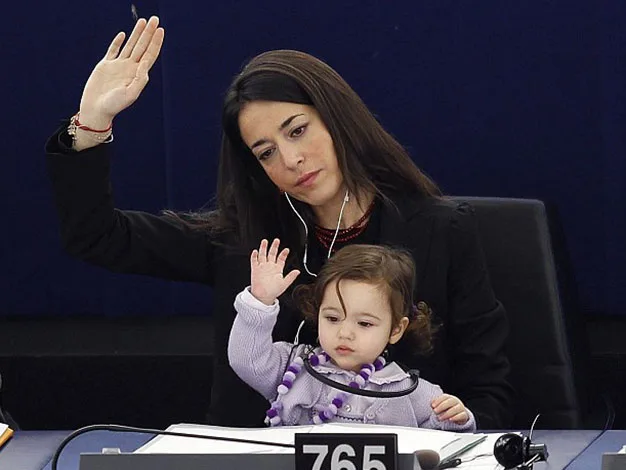 Woman and child sitting, both raising their hands in a formal setting, possibly a meeting or conference.