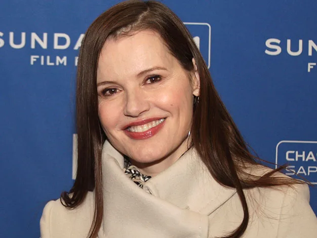 A person smiling in front of a blue Sundance Film Festival backdrop, wearing a light coat.