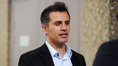 A man in a suit stands outdoors, appearing to be in conversation.
