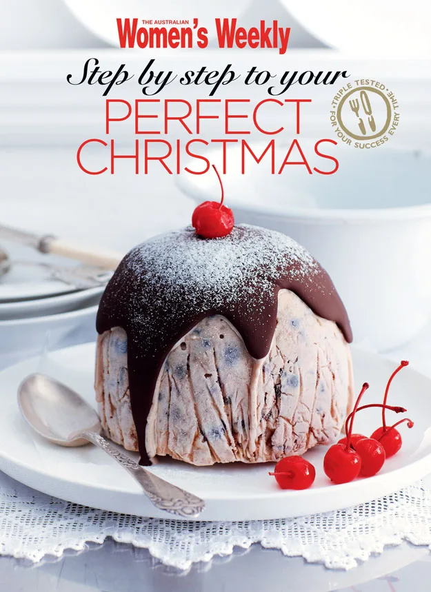 Christmas pudding with chocolate glaze and cherries on a white plate, featured in "Women's Weekly" magazine.