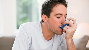 Man using an inhaler for asthma relief while sitting indoors.