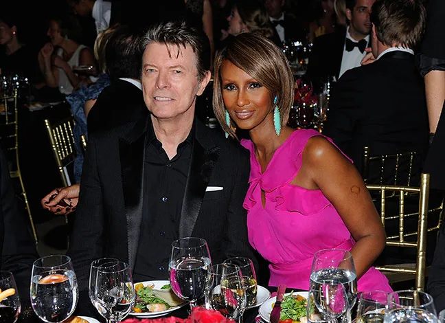 A couple seated at a formal event, surrounded by elegantly set tables with meals and drinks.