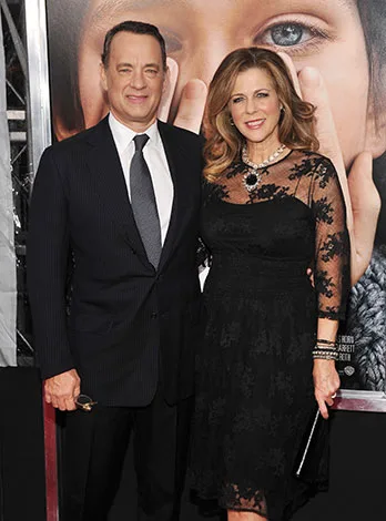 Two people in formal attire posing in front of a movie poster at a film premiere event.