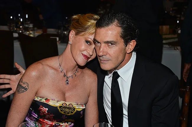 Two people sitting closely at a formal event, the woman in a floral dress and the man in a black suit.