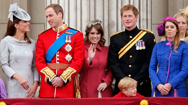 Royal family members on a balcony during a public event, smiling and waving at the crowd.