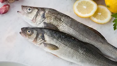 Two fresh fish on a cutting board with lemon slices and herbs.