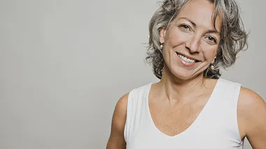 Smiling woman with gray hair in a white top against a neutral background.