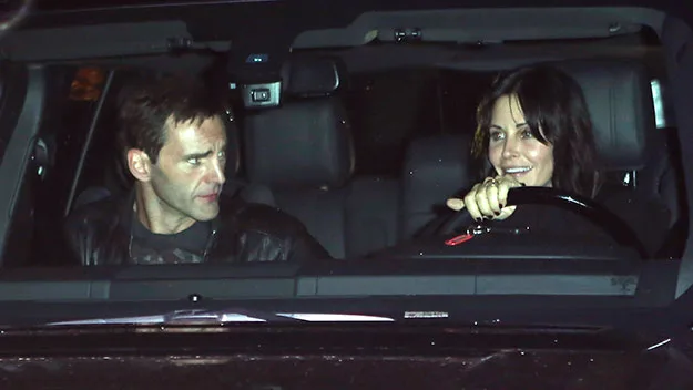 Two people sitting in a car at night, one driving and the other in the passenger seat, engaged in conversation.