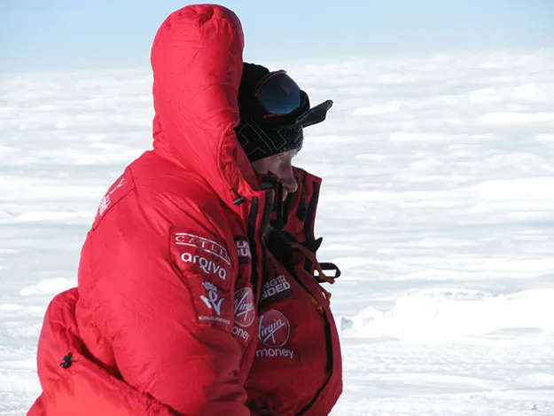 Person in red expedition suit and goggles on snowy terrain during a polar trek.