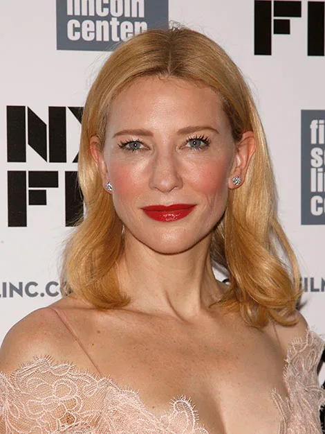 Cate Blanchett at a film event, wearing a lace dress and red lipstick, with branding in the background.