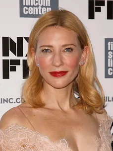Cate Blanchett at a film event, wearing a lace dress and red lipstick, with branding in the background.