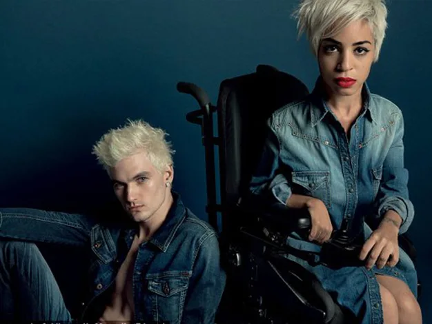 Two individuals with platinum blonde hair, both wearing denim outfits; one is seated in a wheelchair.