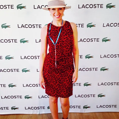 Person in a red leopard-print dress and hat, standing in front of a Lacoste branded backdrop.