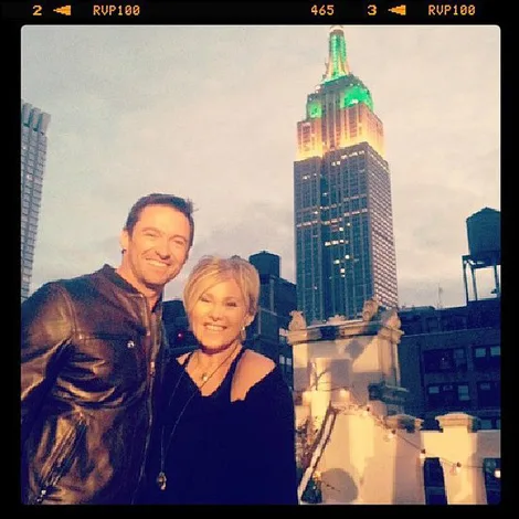 Alt text: "Two people smiling on a rooftop, Empire State Building lit up in background."