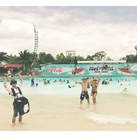 People posing in a wave pool at Wet'n'Wild Gold Coast, with a Coca-Cola sign and roller coaster in the background.