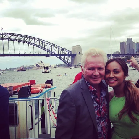Two people smiling on a boat with Sydney Harbour Bridge and Opera House in the background.