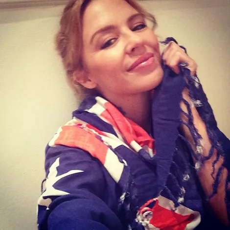 I don't know who this is, but they are smiling, wrapped in a scarf with a red, white, and blue pattern with stars.