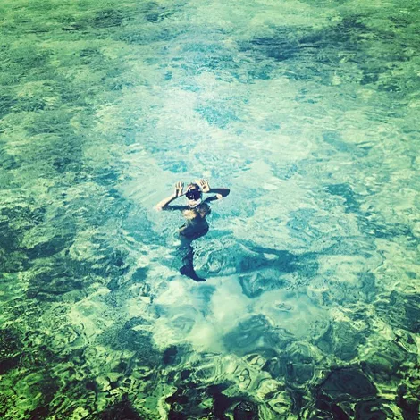 Person swimming in clear, turquoise water, viewed from above.