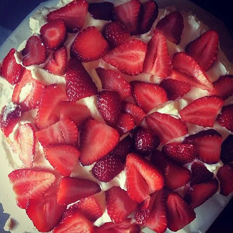 Cake topped with fresh sliced strawberries on a layer of whipped cream.