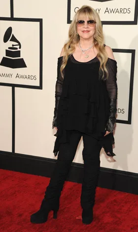 Woman in black outfit on red carpet at the Grammy Awards, standing in front of a backdrop with Grammy logos.