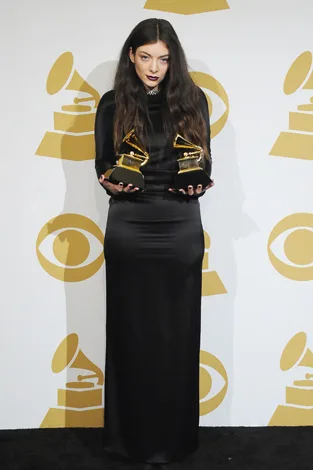 Singer in a black dress holding two Grammy awards against a backdrop with Grammy logos.