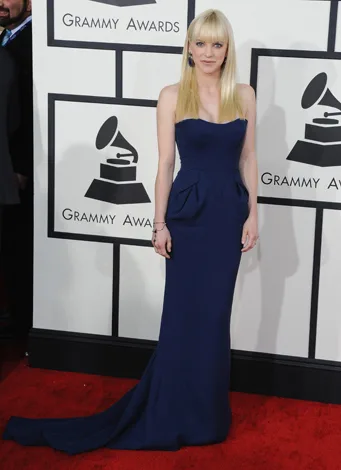Woman in a blue gown poses on the red carpet at the Grammy Awards, with Grammy logos in the background.