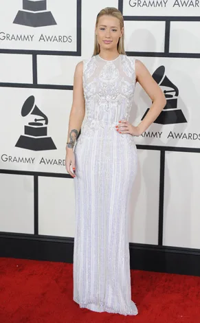Woman in an elegant white gown on the red carpet at the Grammy Awards with a backdrop of Grammy logos.
