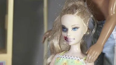 Barbie doll with bruises on face, being held by a Ken doll, highlighting domestic violence awareness.