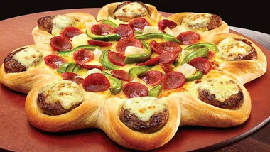 Round pizza with a crust made of stuffed cheeseburgers, topped with pepperoni and green bell peppers.