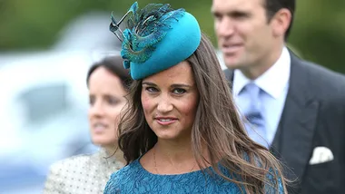 Pippa Middleton smiles at an outdoor event wearing a teal dress and matching fascinator.