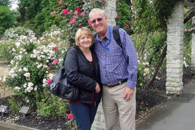 Couple smiling and posing in a garden with blooming roses and greenery in the background.