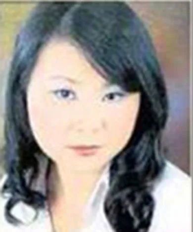 Portrait of a woman with long, dark hair and a white top, against a blurred background.