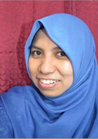 A person smiling, wearing a blue hijab and standing against a red patterned background.