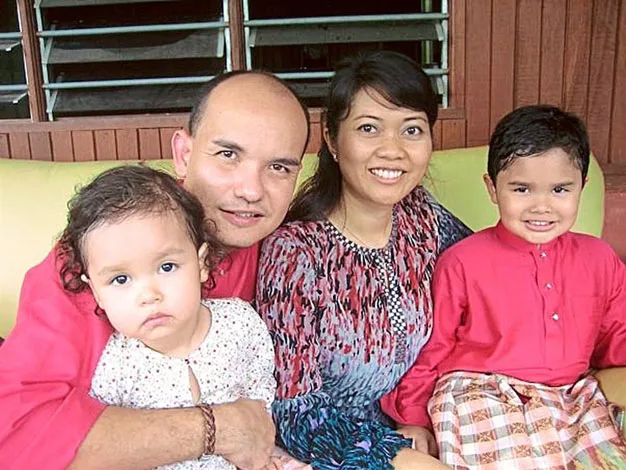 Family of four sitting and smiling, two adults and two children, one wearing a traditional pink outfit.