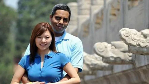 Man and woman in blue shirts standing closely with stone carvings in the background.