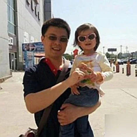 Man holding a child wearing sunglasses outside a building on a sunny day.