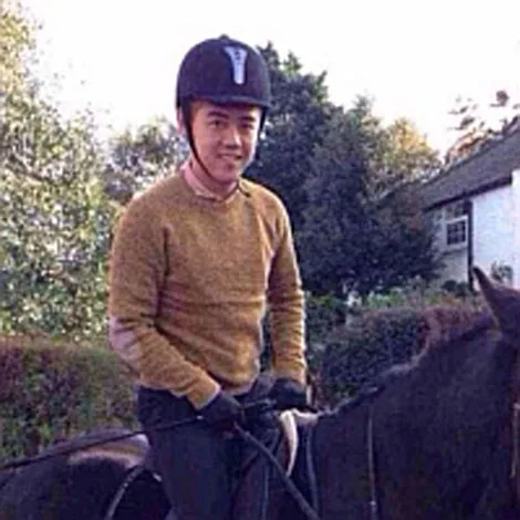 Man in a helmet riding a dark horse outdoors, wearing a brown sweater and gloves.