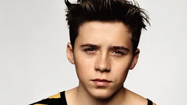 Young male with styled hair, wearing a striped shirt, looking directly at the camera against a plain background.
