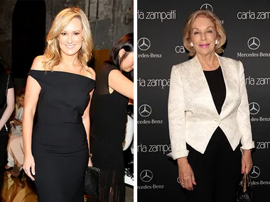 Two women at a fashion event, one in a black dress and the other in a white jacket, smiling at the camera.