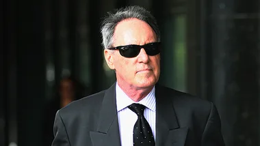 Man in a suit and sunglasses walking outside a building.