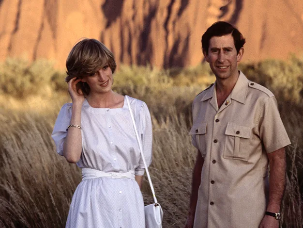 Two people standing in front of Uluru in casual attire, with the woman in a white dress and the man in a beige shirt.