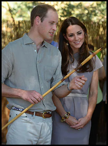 A couple holds a traditional spear, standing together and smiling, with a natural background.