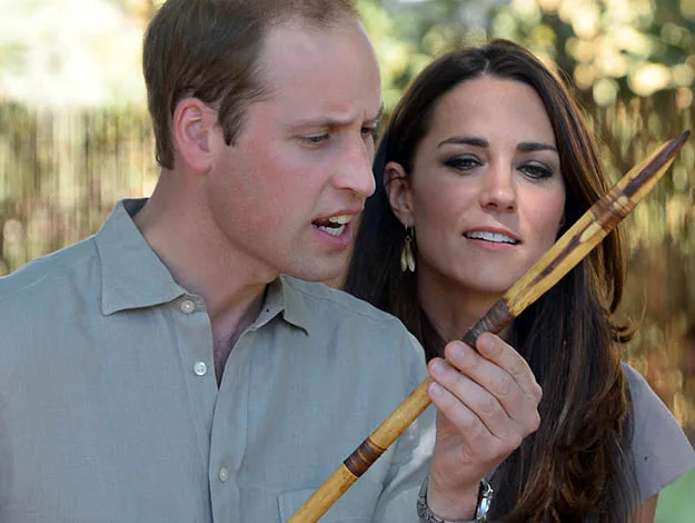 Two people observing a long wooden object closely, with trees blurred in the background.