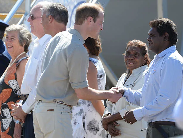 Men shaking hands in a line of people under the sun, with several others engaged in conversation nearby.