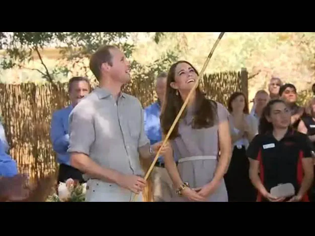Two people outdoors looking up with smiles, surrounded by a group of onlookers in a sunny setting.