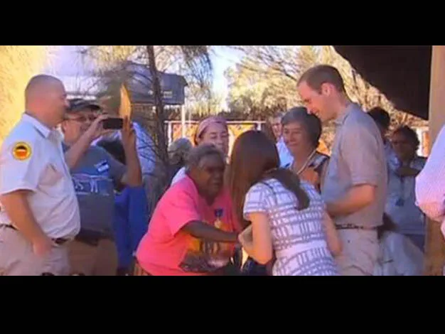 Group of people interacting outdoors, with a woman in a pink shirt greeting a man and a woman. Trees in the background.