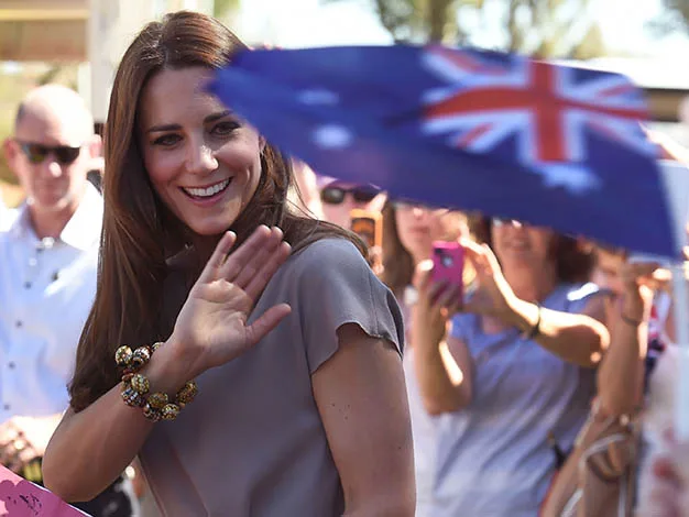 Woman waving amidst crowd, Australian flag in foreground.
